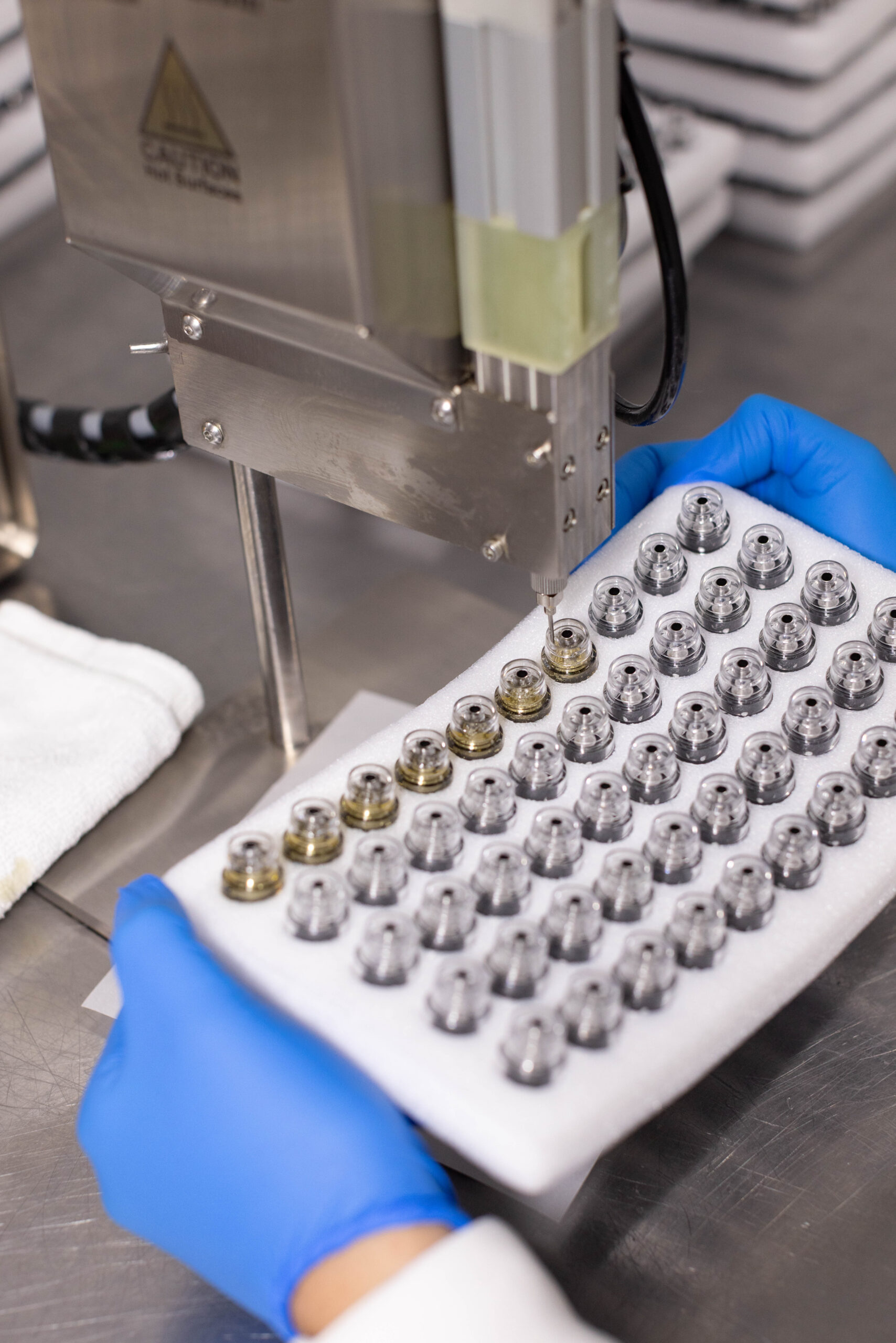 Gloved technician loading vape cartridge tray into filling machine